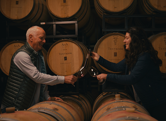 Abigail Horstman Estrada and Jon Pey tasting wine with barrels in background