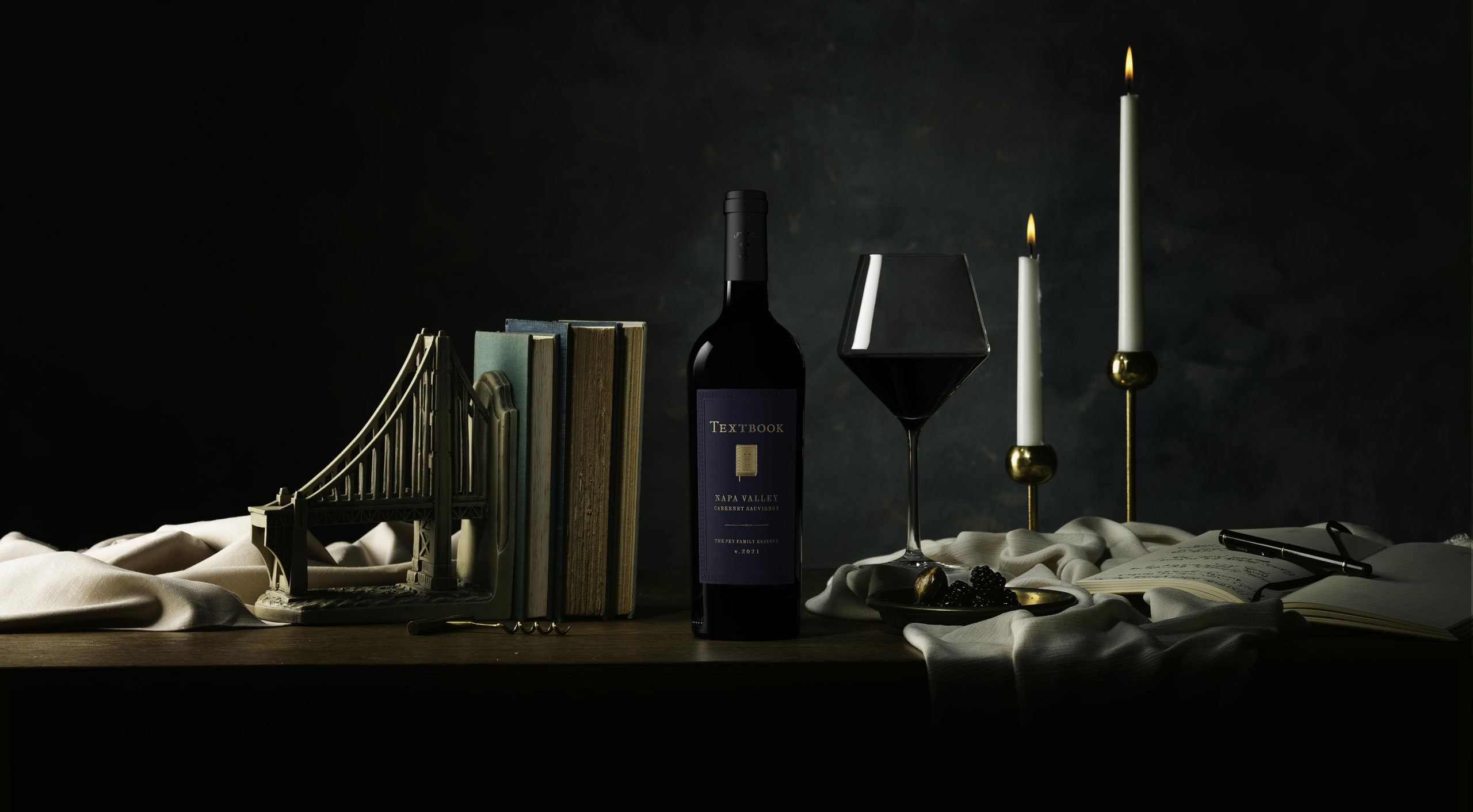 TEXTBOOK Reserve Cabernet bottle on table with books and a glass of red wine