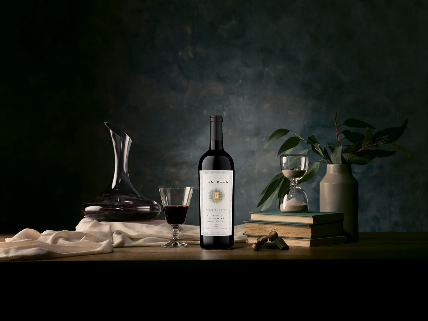 A bottle of Cover to Cover Cabernet surrounded by books, a decanter and wine glass